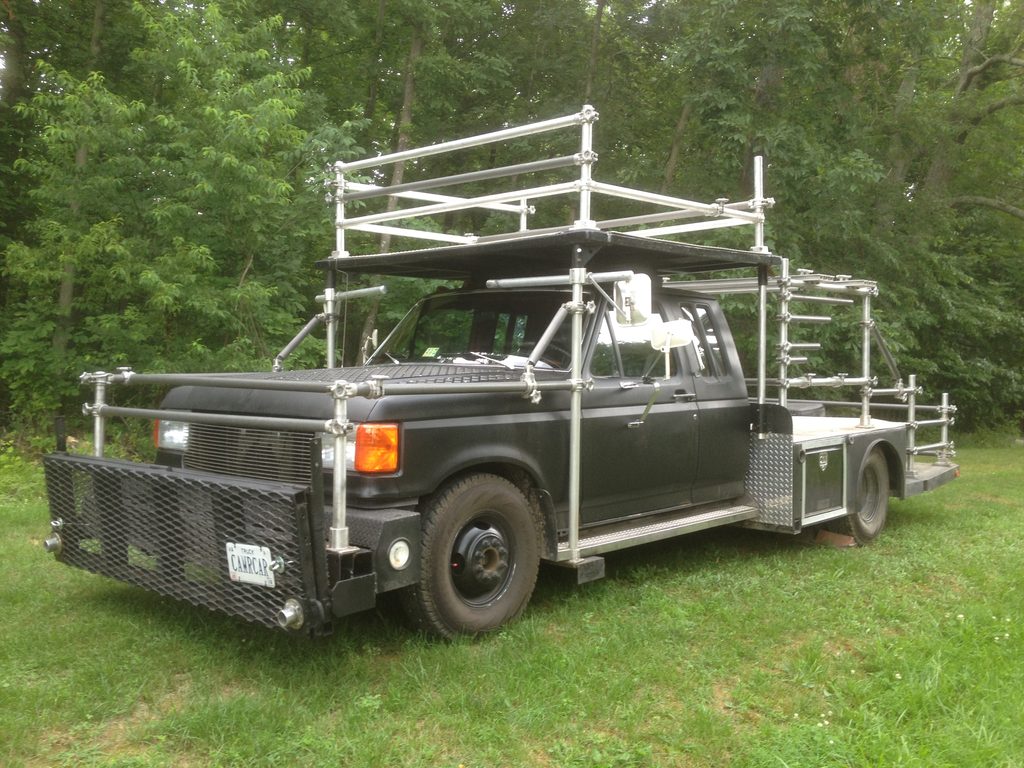 Purpose-built black camera car with an aluminum pipe rig, parked on grass.