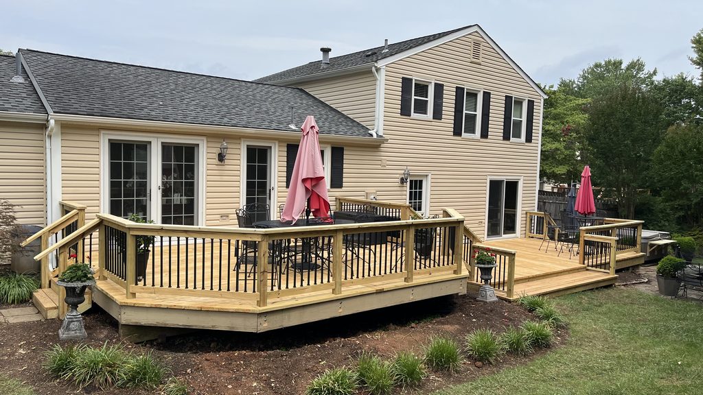 Finished multi-level wraparound pressure-treated deck with black balusters on a tan-sided house.