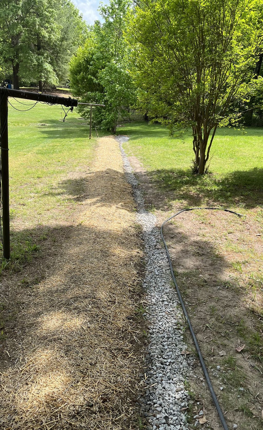 New gravel French drain trench running across a lawn beside a strawed, seeded strip.