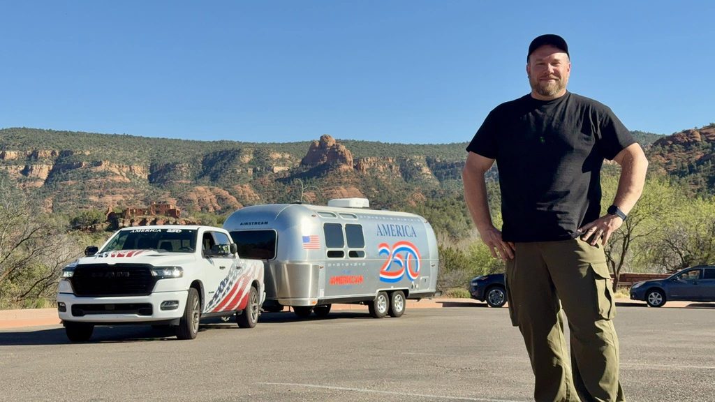 Joey Walker standing in front of a pickup and Airstream trailer with red rock canyon walls behind.