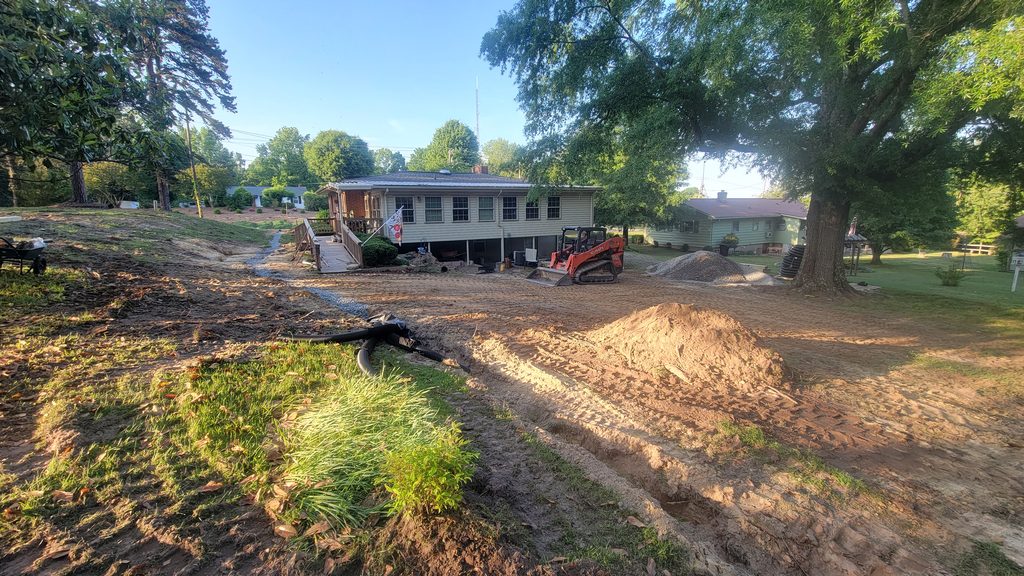 Residential backyard regraded to bare dirt, an orange compact track loader and dirt piles in front of the house.